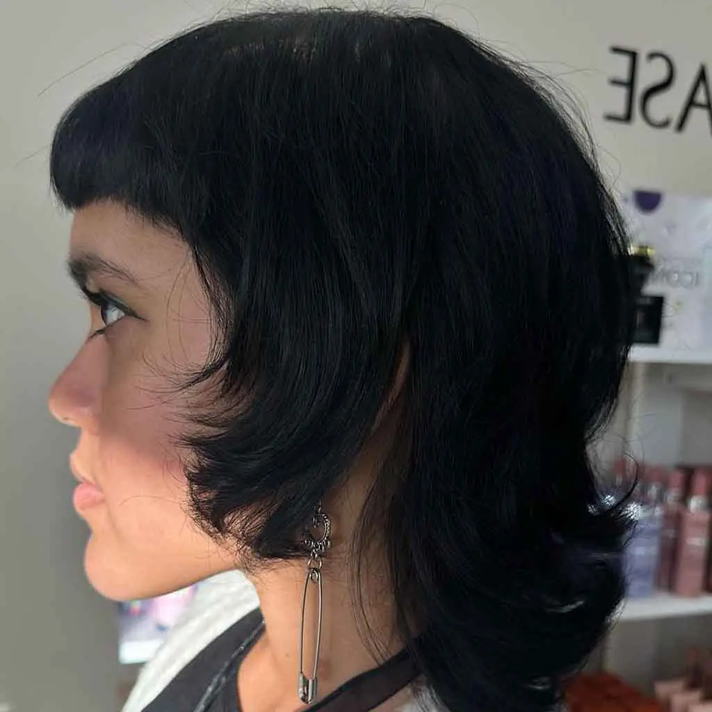 Woman flaunting a black short shag mullet wolf cut with edgy micro bangs, showcasing a bold and modern hairstyle