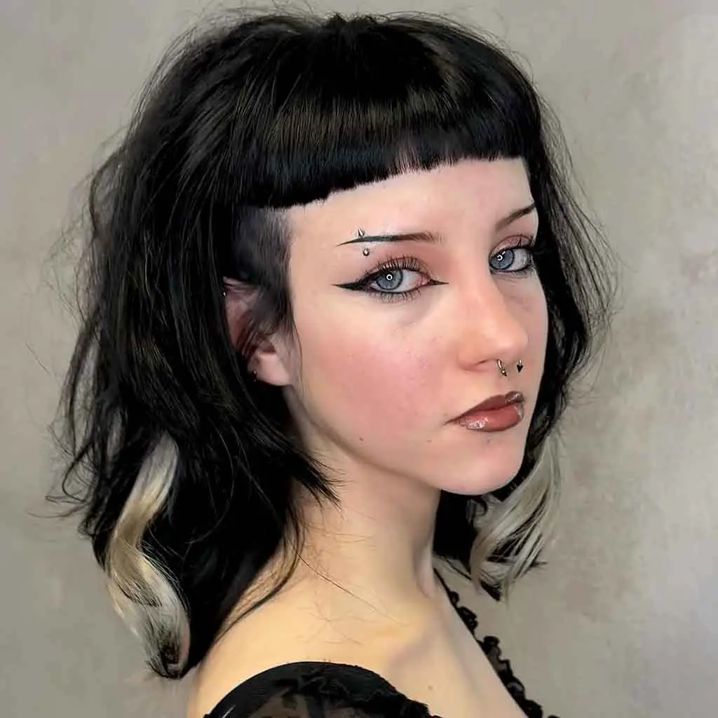 Woman rocking an emo short black mullet wolf cut with an undercut, choppy micro bangs, and blonde highlights for a rebellious look