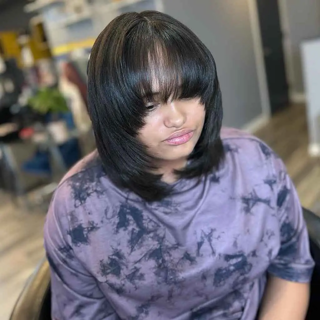 Woman showing off a face-framing bob wolf cut with long choppy bangs on shiny black hair, creating a stylish and textured look
