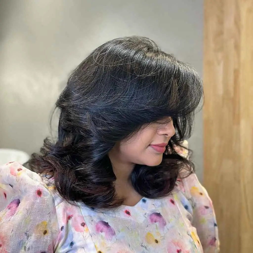 Woman displaying a fluffy wavy medium sable black wolf cut with wavy curtain bangs, adding volume and softness