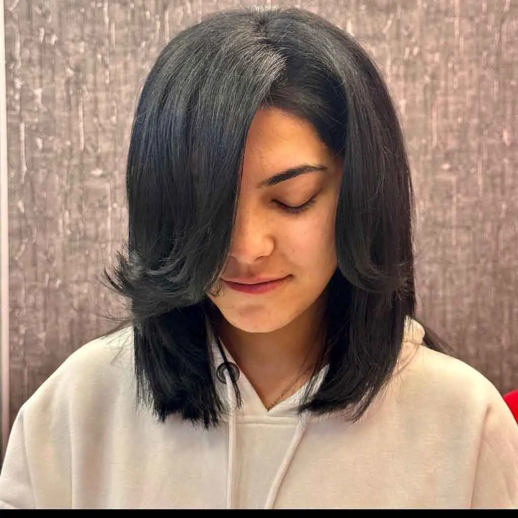 Woman showcasing an ink black thick medium wolf cut on straight hair with long wavy side-swept bangs, blending volume and elegance