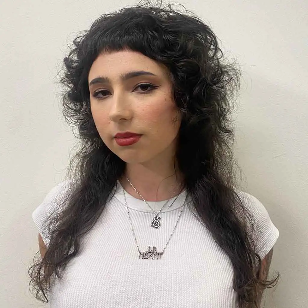 Woman rocking a long curly black mullet wolf cut with blunt micro bangs, blending boldness with natural curls