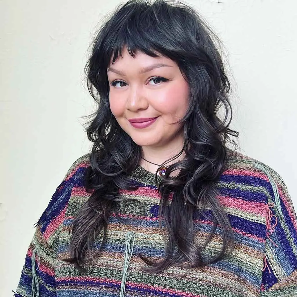 Woman showcasing a long wavy black pearl mullet wolf cut with asymmetric bangs, creating a bold and trendy effect