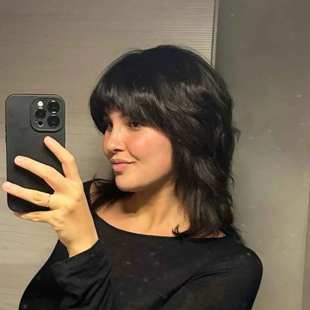 Woman showing off a medium ebony black fluffy mullet wolf cut with asymmetric bangs, adding edgy and playful texture
