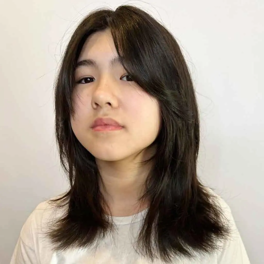 Woman showcasing a medium wolf cut with curtain bangs on crow black hair, featuring soft layers for a chic, voluminous look