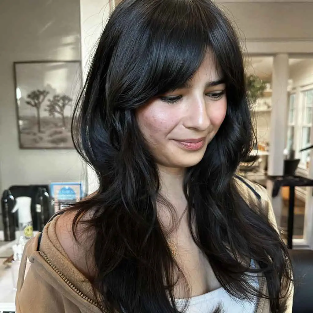 Woman flaunting a rich black long wavy layered wolf cut with curtain bangs, enhancing movement and depth