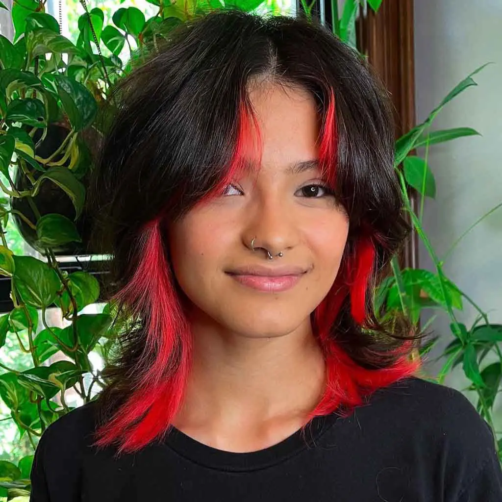 Woman flaunting a short wavy wolf cut with curtain bangs and orange-red chunky highlights, adding a fiery and vibrant touch