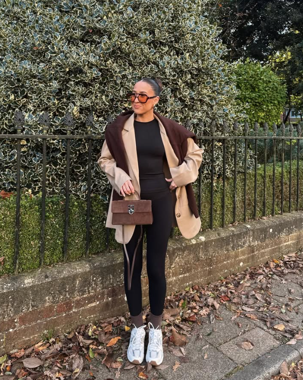 beige coat over a black outfit with a brown sweater draped over her shoulders