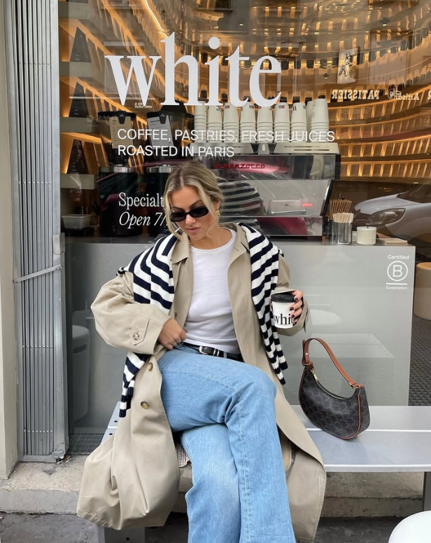 beige trench coat a striped sweater draped over their shoulders a white shirt and light blue jeans