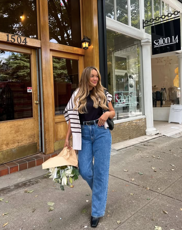 black top blue jeans and has a striped sweater draped over her shoulders