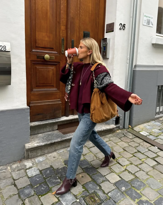 burgundy jacket with patterned sleeves blue jeans and brown ankle boots carrying a large tan bag