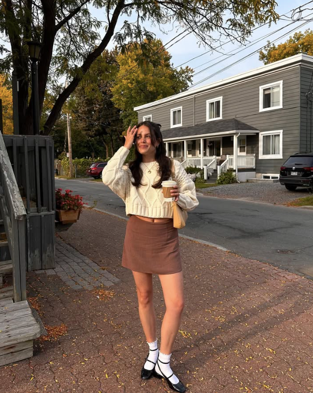 cream sweater and brown skirt holding a coffee cup