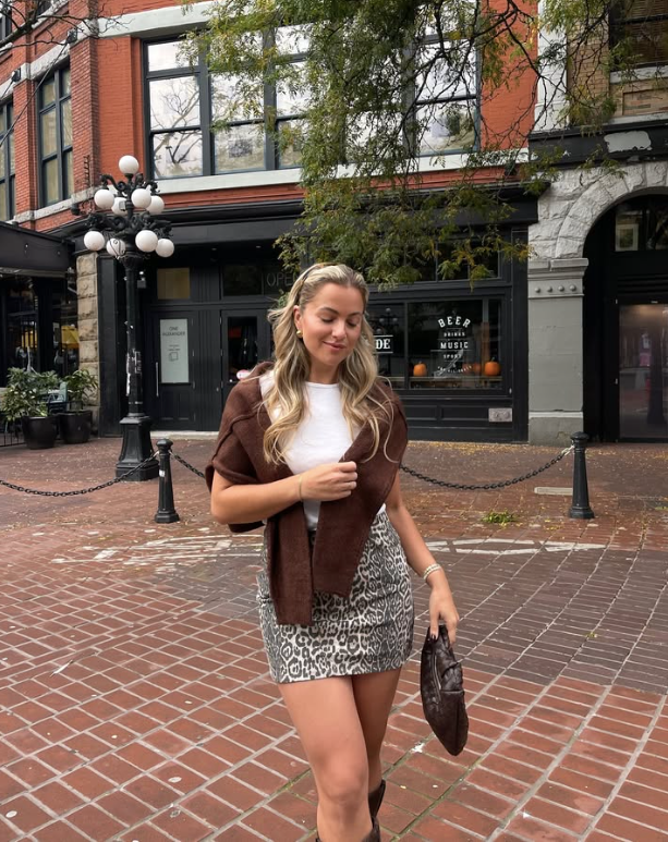 white shirt brown sweater draped over her shoulders and a leopard print skirt