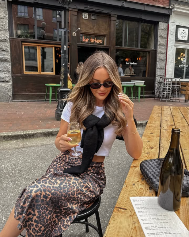 white top a black sweater draped over her shoulders and a leopard print skirt